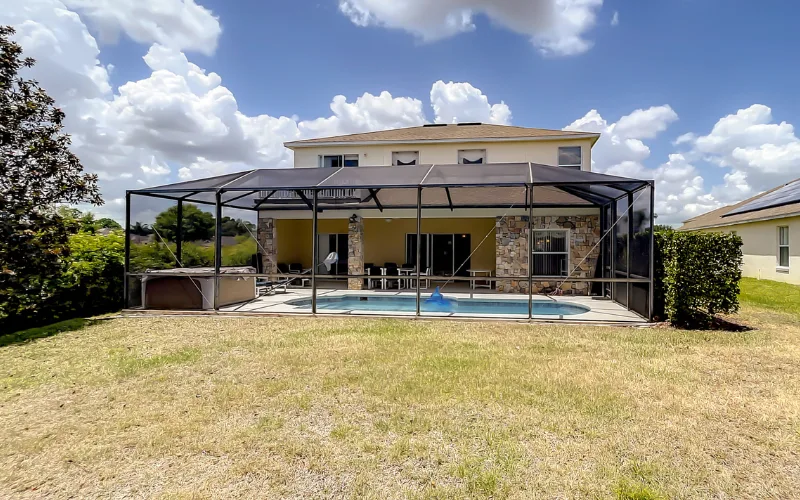 Rear exterior of villa with screened pool enclosure and lawn